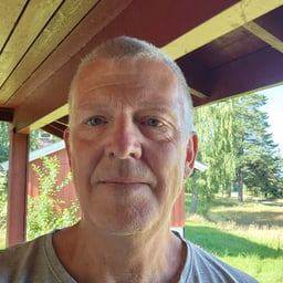 A middle-aged man with short gray hair looks at the camera outdoors.